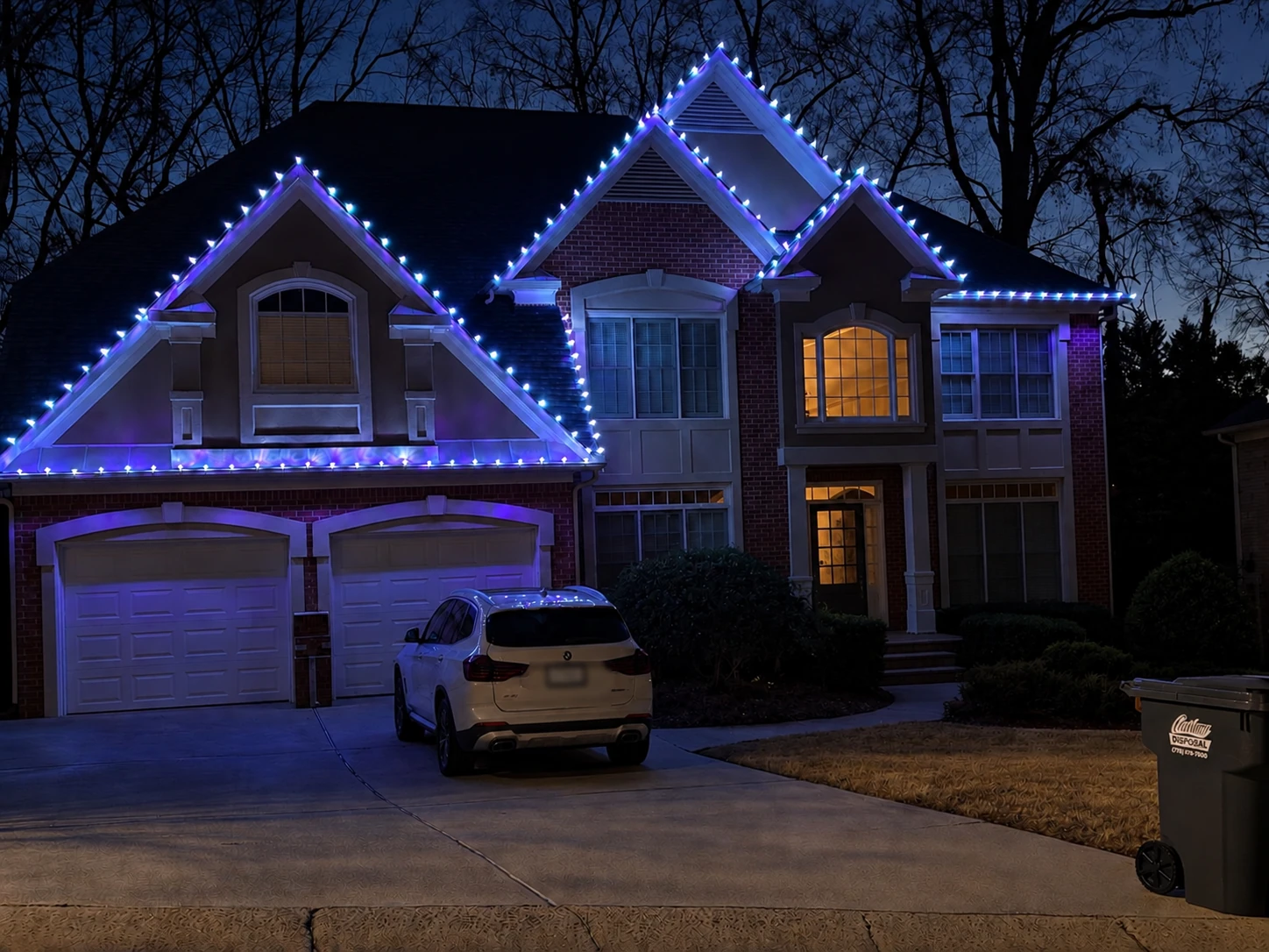 A two-story home outlined with cool white and blue Christmas lights